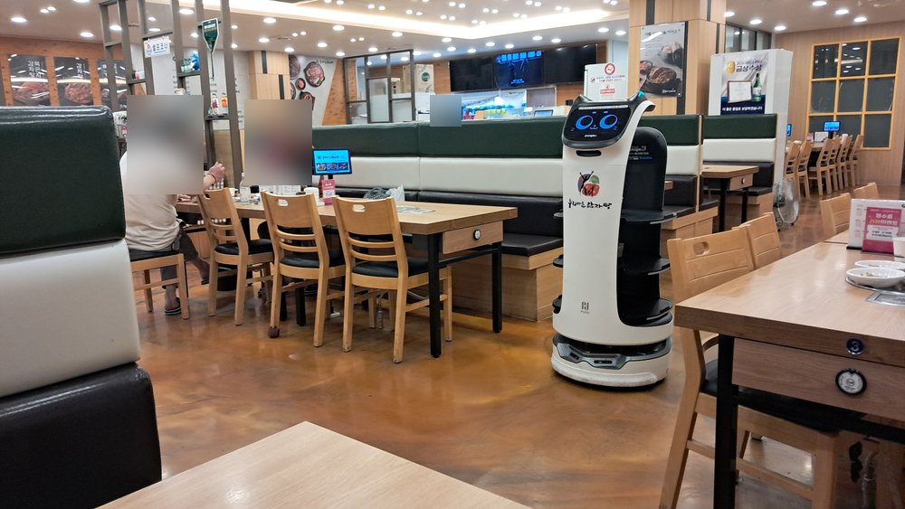 A machine that walks, or rolls, photographed on the Other Side among the chairs. It has not been told about the chairs.